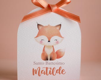 May include: A white arched favor box topped with a peach-colored satin ribbon bow. The front features a watercolor illustration of a fox with closed eyes and pink cheeks, with the text Santo Battesimo and the name Matilde printed below it.