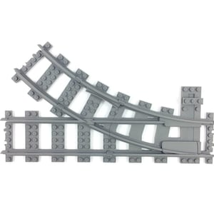 Op de afbeelding: Grijze plastic speelgoedtreinrails met een gebogen gedeelte en een wissel. De rails zijn ontworpen om aan te sluiten en een speelgoedtrein van richting te laten veranderen. Witte achtergrond.