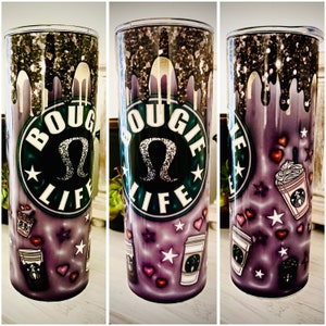 May include: A stainless steel tumbler with a purple and black design. The tumbler features a gold glitter design with a dripping effect. The tumbler has a white circle with the text "BOGIE LIFE" and a black and silver Lululemon logo. The tumbler is surrounded by a purple background with white stars, hearts, and coffee cups.