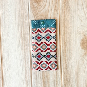 May include: A small, rectangular pouch with a teal and white polka dot fabric top and a colorful geometric pattern on the bottom. The pouch is made of fabric and has a button closure.