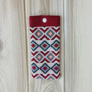 May include: A red and white fabric phone case with a geometric pattern. The case has a white button on the top.