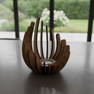 Puede incluir: Un portavelas de madera con un diseño único y abierto. El portavelas presenta listones de madera verticales y curvados dispuestos en un patrón circular, creando una forma de flor. Una pequeña vela blanca se encuentra en el centro. El portavelas es de madera marrón claro.