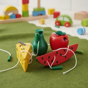 May include: A wooden toy set including a yellow cheese wedge with a mouse, a green pear, a red apple, and a red watermelon slice. Each piece has a string for threading. Other wooden toys are in the background.
