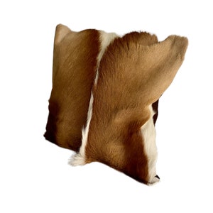 May include: A brown and white cowhide pillow with a soft, fuzzy texture.