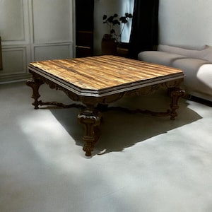 Op de afbeelding: Een grote, vierkante, houten salontafel met ingewikkelde houtsnijwerk op de poten en een donkerbruin houten blad.
