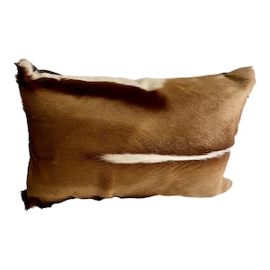 May include: A brown and white animal hide pillow with a rectangular shape. The pillow has a soft, fuzzy texture.