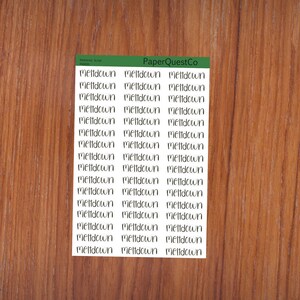 Op de afbeelding: Een vel stickers met het woord "meltdown" dat meerdere keren wordt herhaald in een handschriftlijk lettertype. De stickers zijn wit en bevinden zich op een houten achtergrond.