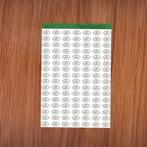 May include: A sheet of white sticker labels with the word "GRE" printed in black inside a hexagon shape. The sheet is on a wood surface.