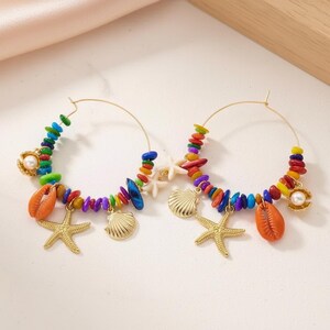 May include: Gold hoop earrings adorned with colorful beads, seashells, starfish, and pearls. The earrings feature a vibrant array of colors, including orange, blue, green, and yellow, creating a beach-inspired aesthetic.