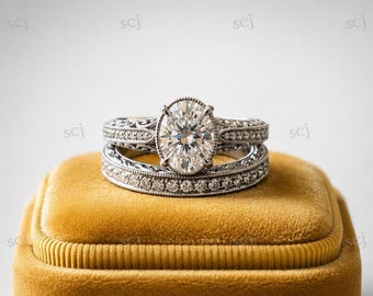 May include: A silver-toned engagement ring set featuring an oval-cut center stone surrounded by a halo of small round stones. The bands are crafted with intricate milgrain detailing and pavé-set stones along the shank, creating a cohesive look.