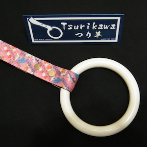 Puede incluir: Anillo de cerámica blanca con una correa de tela estampada en rosa y azul. La correa tiene detalles metálicos dorados y el texto "Tsurikawa つり革 MADE FOR RIDE" está impreso en una etiqueta azul.