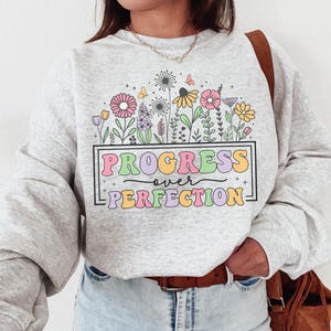 May include: A gray sweatshirt with a graphic of colorful flowers and the text "Progress over Perfection".