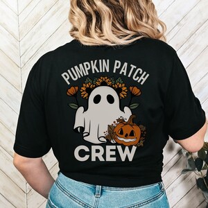 May include: Black t-shirt with a Halloween-themed graphic. The design features a friendly ghost, a jack-o'-lantern, and the text "PUMPKIN PATCH CREW" in a circular arrangement. The design includes sunflowers and fall foliage.