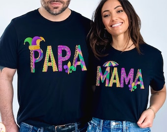May include: Black t-shirts with the words "PAPA" and "MAMA" in colorful, patterned letters. The "PAPA" shirt features a jester hat and fleur-de-lis, while the "MAMA" shirt has an umbrella and fleur-de-lis. The shirts are a matching set.