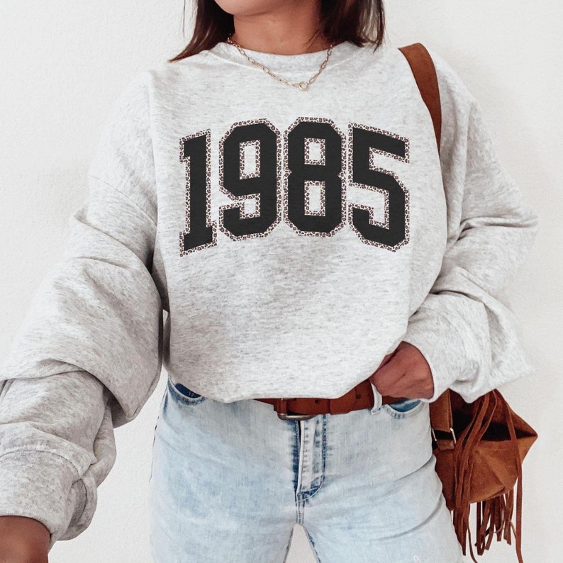 May include: Gray sweatshirt with a black and brown leopard print 1985 design.
