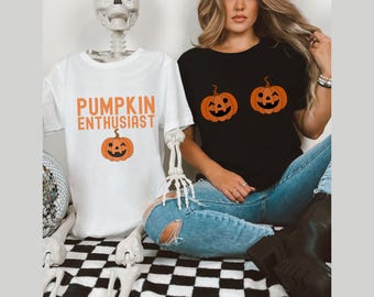 May include: Two t-shirts with pumpkin designs. One white t-shirt says "Pumpkin Enthusiast" with a smiling pumpkin. The other black t-shirt has two smiling pumpkins.