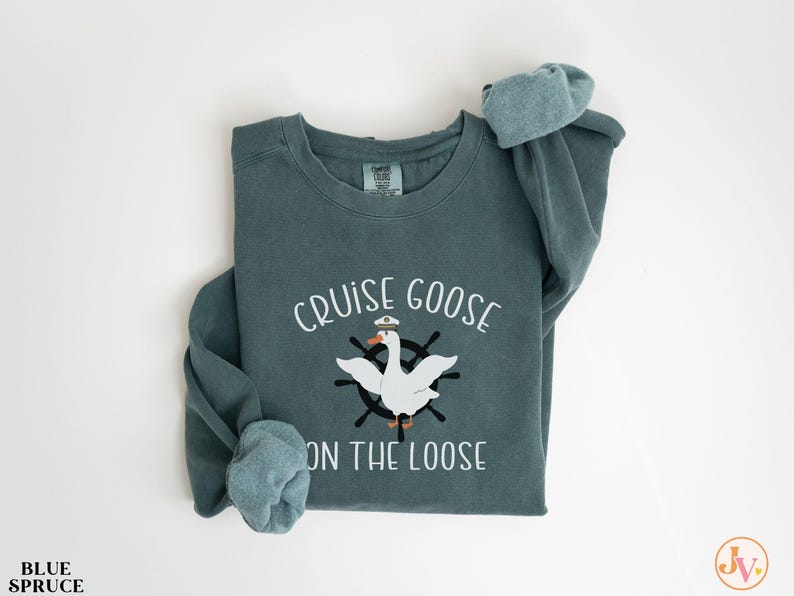 Puede incluir: Una sudadera azul verdosa con el texto "Cruise Goose on the Loose" y un dibujo animado de un ganso con un sombrero de capit&aacute;n y un volante.