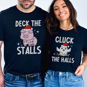 Peut inclure: Deux t-shirts noirs avec un motif sur le th&egrave;me de No&euml;l. Le premier t-shirt repr&eacute;sente un cochon portant un chapeau de P&egrave;re No&euml;l et le texte "Deck the Stalls". Le deuxi&egrave;me t-shirt repr&eacute;sente un poulet portant un chapeau de P&egrave;re No&euml;l et le texte "Cluck the Halls".