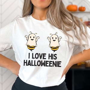 May include: White t-shirt with a graphic of two ghosts dressed as bees. The text "I love his Halloweenie" is printed below the ghosts.