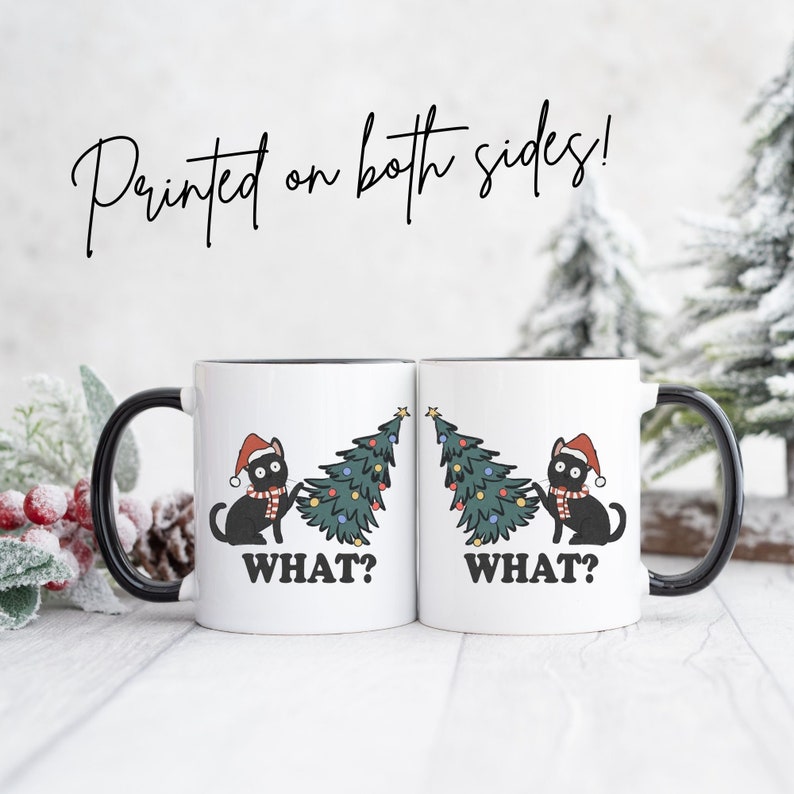 May include: Two white ceramic mugs with black handles. Each mug features a black cat wearing a Santa hat and pulling on a Christmas tree. The text "WHAT?" is printed on each mug.