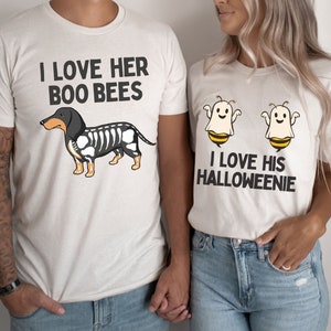 May include: Two white t-shirts with a Halloween-themed couple's design. The first shirt features a black and white dachshund with the text "I love her boo bees". The second shirt features two ghost bees with the text "I love his Halloweenie".