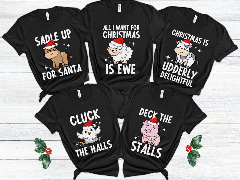 Peut inclure: Cinq t-shirts noirs avec des jeux de mots sur les animaux sur le th&egrave;me de No&euml;l. Les t-shirts pr&eacute;sentent une vache, un mouton, un poulet, un cochon et un cheval, chacun portant un chapeau de P&egrave;re No&euml;l et des lumi&egrave;res de No&euml;l. Le texte sur les t-shirts est : "Saddle Up For Santa", "All I Want For Christmas Is Ewe", "Christmas Is Udderly Delightful", "Cluck The Halls", et "Deck The Stalls".