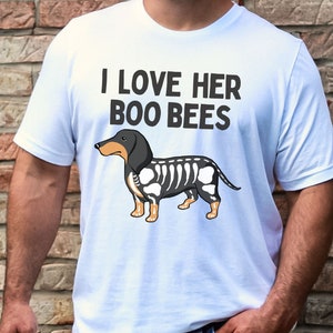 May include: White t-shirt with the text "I love her boo bees" and a cartoon image of a black and white dachshund with a skeleton design.