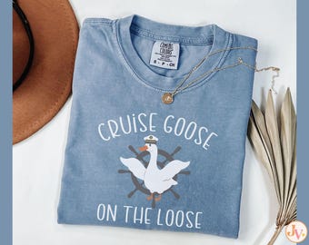 May include: A light blue t-shirt with a white graphic of a goose wearing a captain's hat and a life preserver. The text "Cruise Goose on the Loose" is printed in white on the shirt.