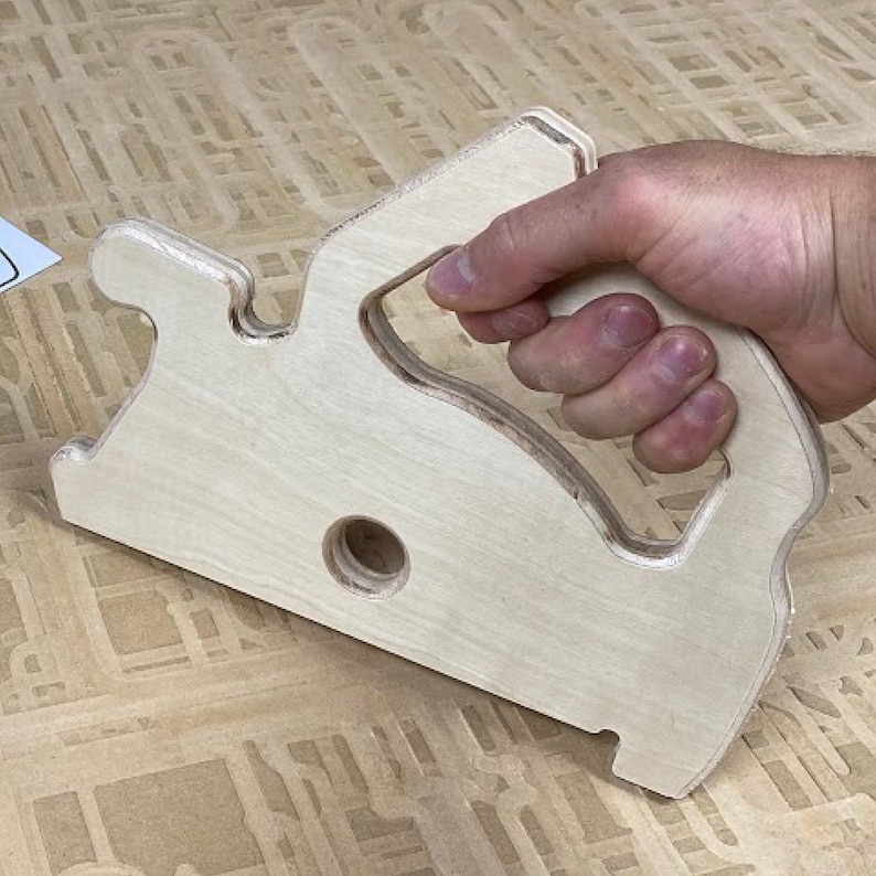 May include: A wooden hand-held tool with a handle and a large, rounded, cut-out shape. The tool is made of light-colored wood and has a hole in the center.