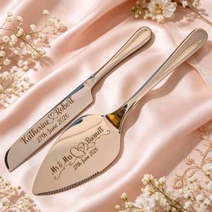 Può includere: Un set di coltello e paletta per torta argentati con testo inciso. Il coltello recita "Katherine Robert 27 giugno 2026" e la paletta recita "Mr & Mrs Burnett 27 giugno 2026". Il set poggia su una superficie di raso rosa.