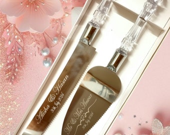 May include: A wedding cake knife and server set with clear acrylic handles and silver blades. The knife and server are engraved with names and a date. The set is presented in a white box with a pink floral background.