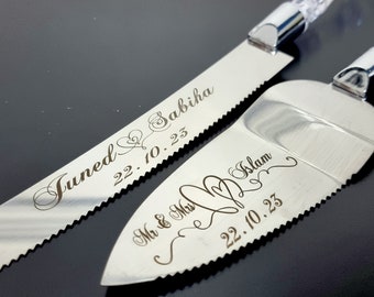 May include: A silver cake knife and server set. The knife is engraved with "Juned & Sabiha" and the date "22.10.23". The server is engraved with "Mr & Mrs Islam" and the date "22.10.23". Both have clear crystal handles.
