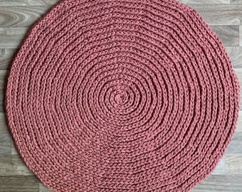 May include: A round, crocheted rug in a dusty rose color. The rug has a circular pattern with concentric circles.