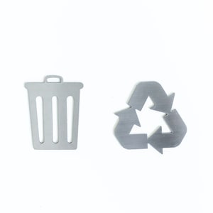 May include: Two metal icons on a white background. The icon on the left is a trash can with a lid. The icon on the right is a recycle symbol with three arrows.