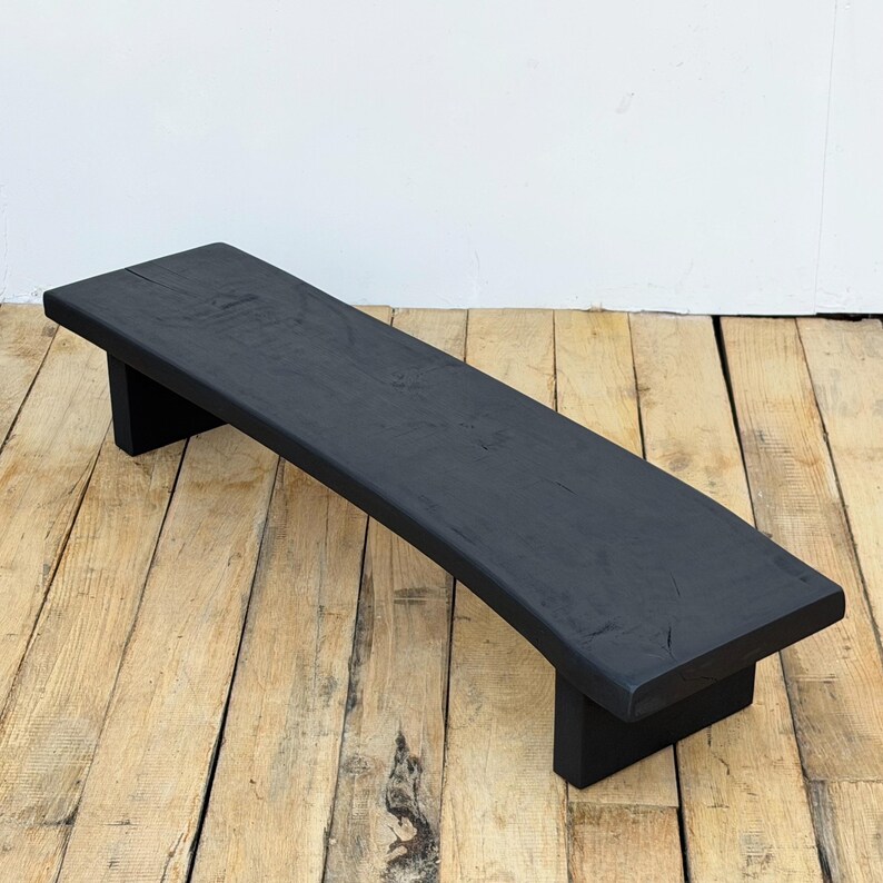 May include: A black wooden bench with a curved seat and two rectangular legs. The bench is painted black and appears to be made of solid wood. The bench is approximately 48 inches long.