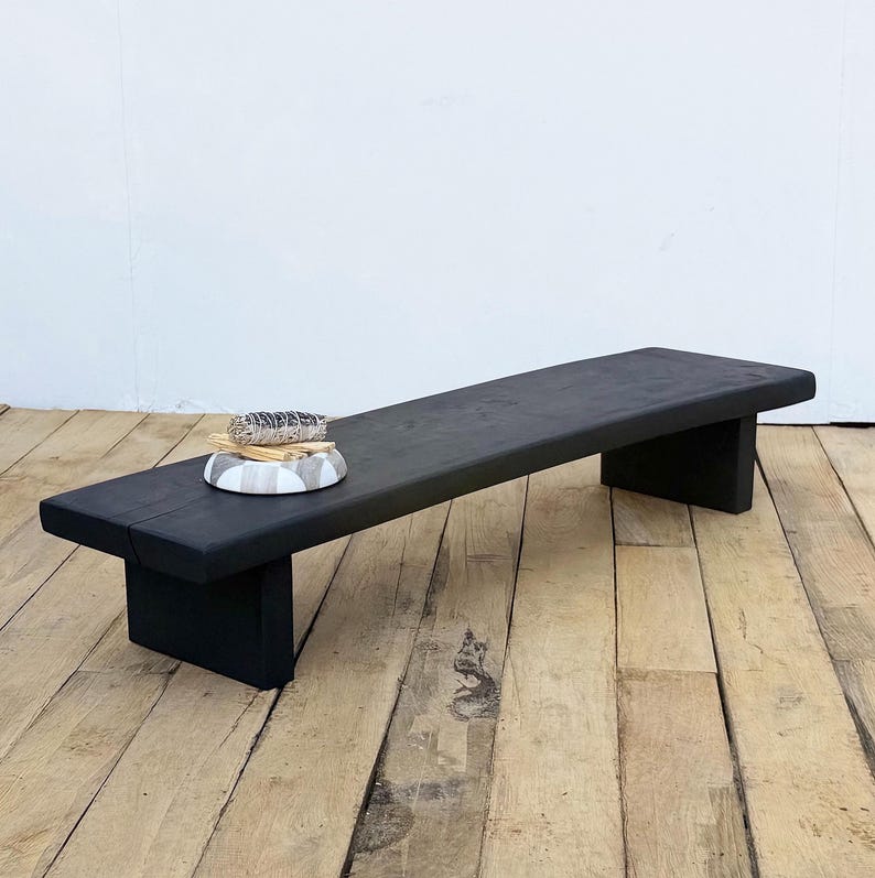 May include: A black wooden bench with a rectangular top and two block legs. A small, round, decorative bowl with a sage bundle and sticks sits on the bench. The bench is made of solid wood and has a matte finish.
