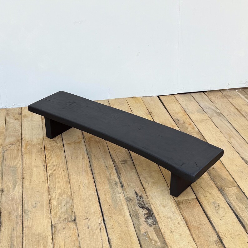 May include: A black, rectangular wooden step stool. The stool is painted black and has a simple, minimalist design. It is elevated on two short legs, and is suitable for various uses.
