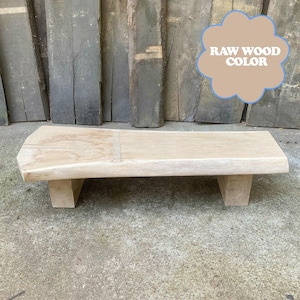 Puede incluir: Un banco de madera rectangular de color claro con dos patas cortas y cuadradas. El banco tiene un acabado de madera natural en bruto. El texto "RAW WOOD COLOR" se muestra en un gráfico en forma de nube.