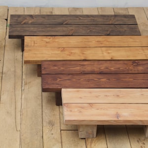Op de afbeelding: Een verzameling houten display verhogers in verschillende bruintinten, van donker tot licht. Elke verhoger is rechthoekig met een platte bovenkant en een stevige basis, die de natuurlijke houtnerf laat zien.