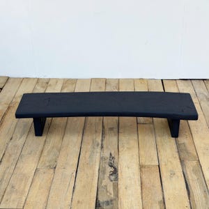 May include: A black wooden riser shelf with a curved top and two supporting legs. The shelf is painted black and sits on a wooden floor. The shelf is approximately 30 inches long.