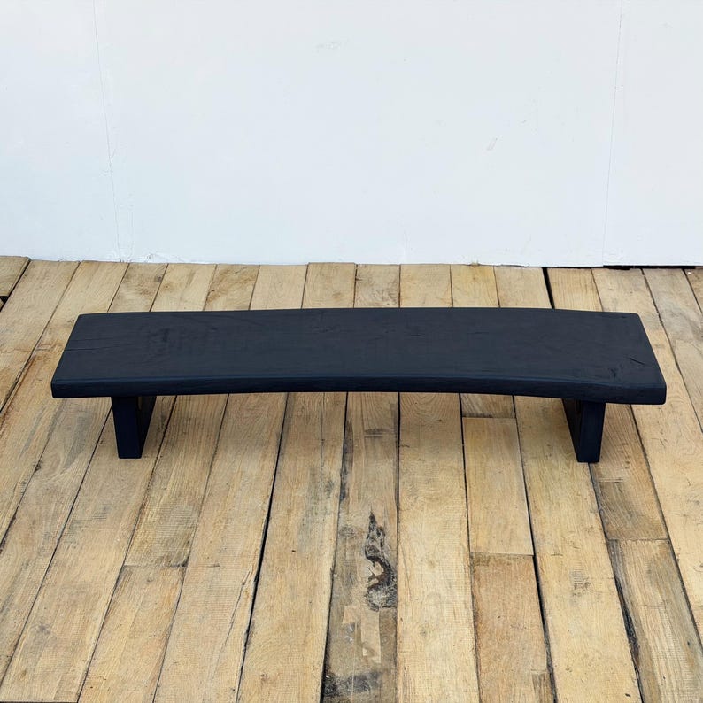 May include: A black wooden riser shelf with a curved top and two supporting legs. The shelf is painted black and sits on a wooden floor. The shelf is approximately 30 inches long.