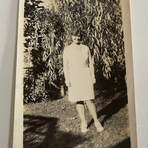 1950’s photo of a stunning lady standing in front of foliage