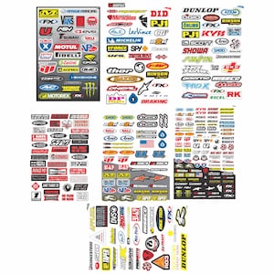 May include: A collection of motorcycle and racing-themed stickers featuring various brand logos and graphics. The stickers are in various shapes and sizes, with a mix of colors including red, white, black, and blue. Brands include Dunlop, Motul, and Ogio.