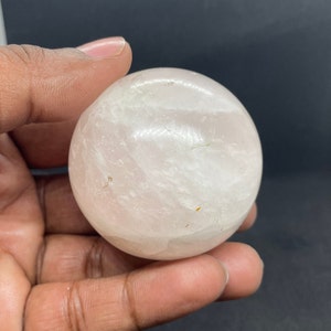 May include: A smooth, white, polished sphere of selenite crystal. The sphere is translucent and has a slight pink hue.