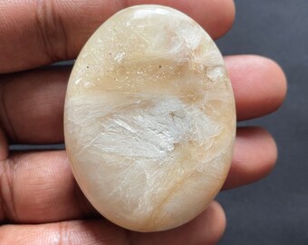 May include: A smooth, oval-shaped, light brown and white gemstone with a swirling pattern.