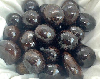 May include: A collection of tumbled dark brown and black gemstones. The stones are smooth and polished, with a glossy finish.