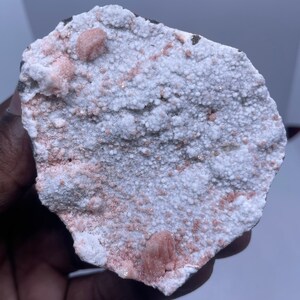 Op de afbeelding: Een witte steen met kleine roze kristallen en een ruwe textuur.