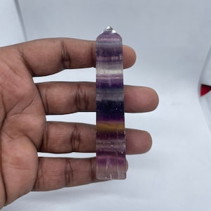 Könnte beinhalten: Eine violette, weiße und goldene Fluorit-Kristallspitze. Der Kristall ist etwa 12,5 cm lang und hat eine spitze Spitze.