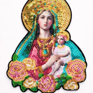 May include: A religious icon featuring a woman holding a child, adorned with gold sequins and surrounded by pink roses. The woman wears a pink dress and a gold halo. The image has a black border.