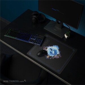 May include: A black computer desk setup with a backlit keyboard, mouse, and mousepad featuring a blue and white graphic. A black monitor and headphones are also visible. The desk is dark, and the overall theme is gaming.